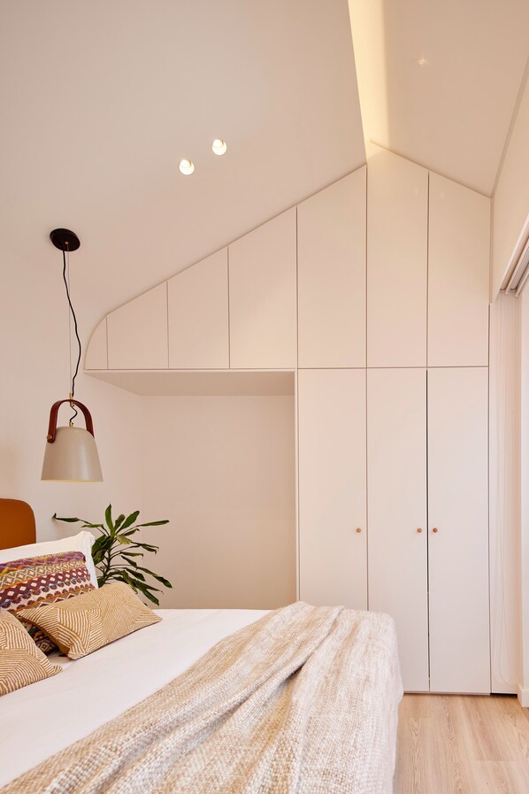 Een slaapkamer met een bed, een hanglamp, een kamerplant en ingebouwde kasten.