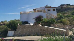 A coastal building with a stone wall, a staircase, and a vehicle parked in front.