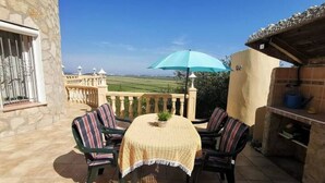A patio with a table, chairs, a blue umbrella, and a stone wall.
