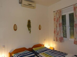 Quarto com cama, ar condicionado, janela com cortinas e luminárias fixadas na parede.
