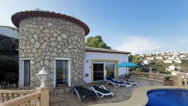 A stone building with a pool, lounge chairs, and a view of the landscape.