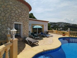 Uma área de piscina com espreguiçadeiras, um edifício de pedra e vista para uma colina.