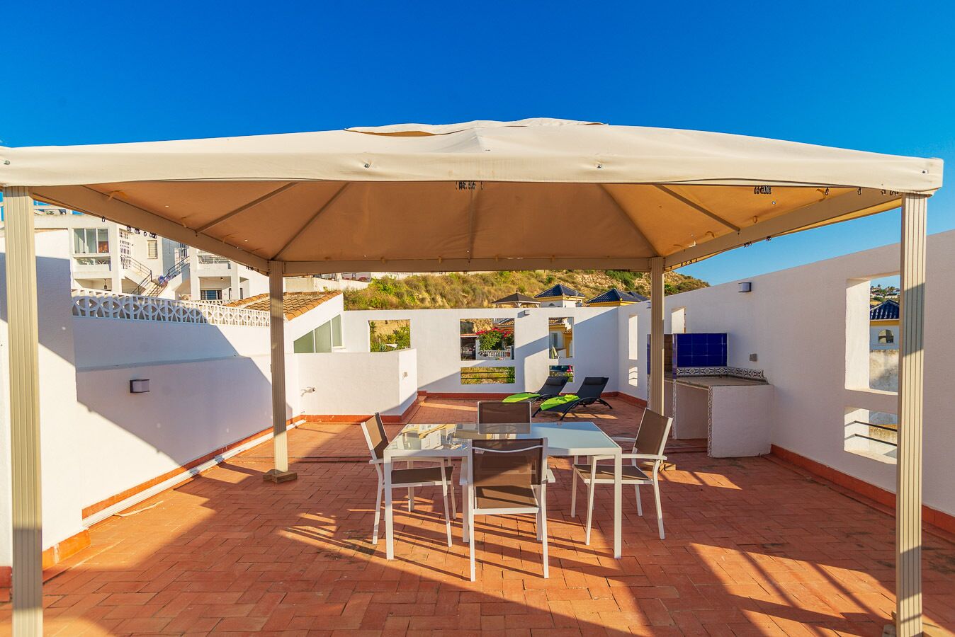 A rooftop patio with a table and chairs, a barbecue area, and a white canopy.