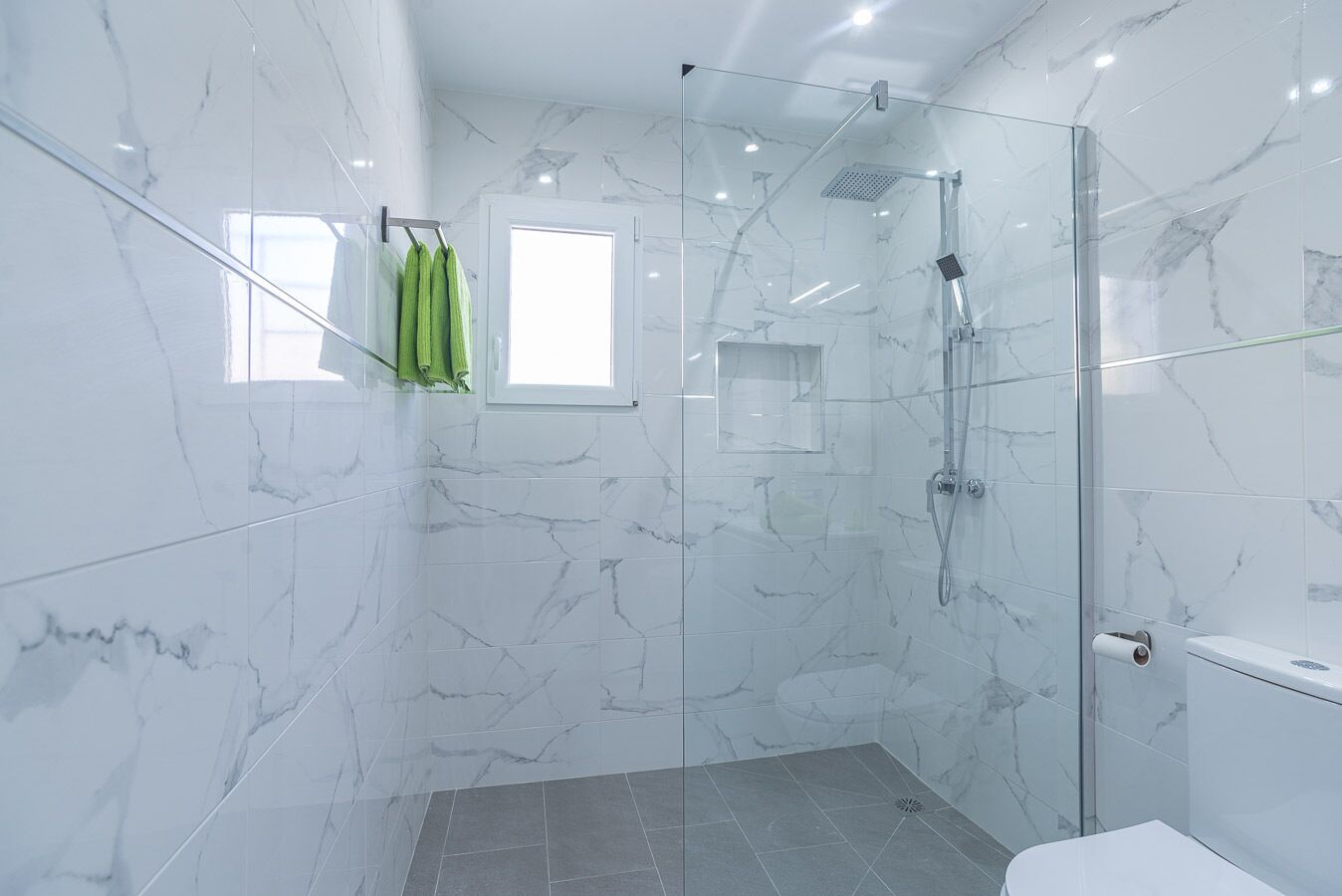 A modern bathroom with marble walls, a glass shower enclosure, and a small window.