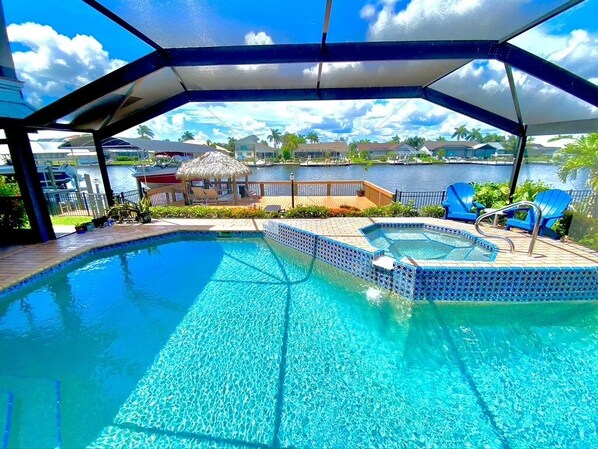 Une piscine avec un jacuzzi, des chaises longues et une vue sur l’eau et les bâtiments en arrière-plan.