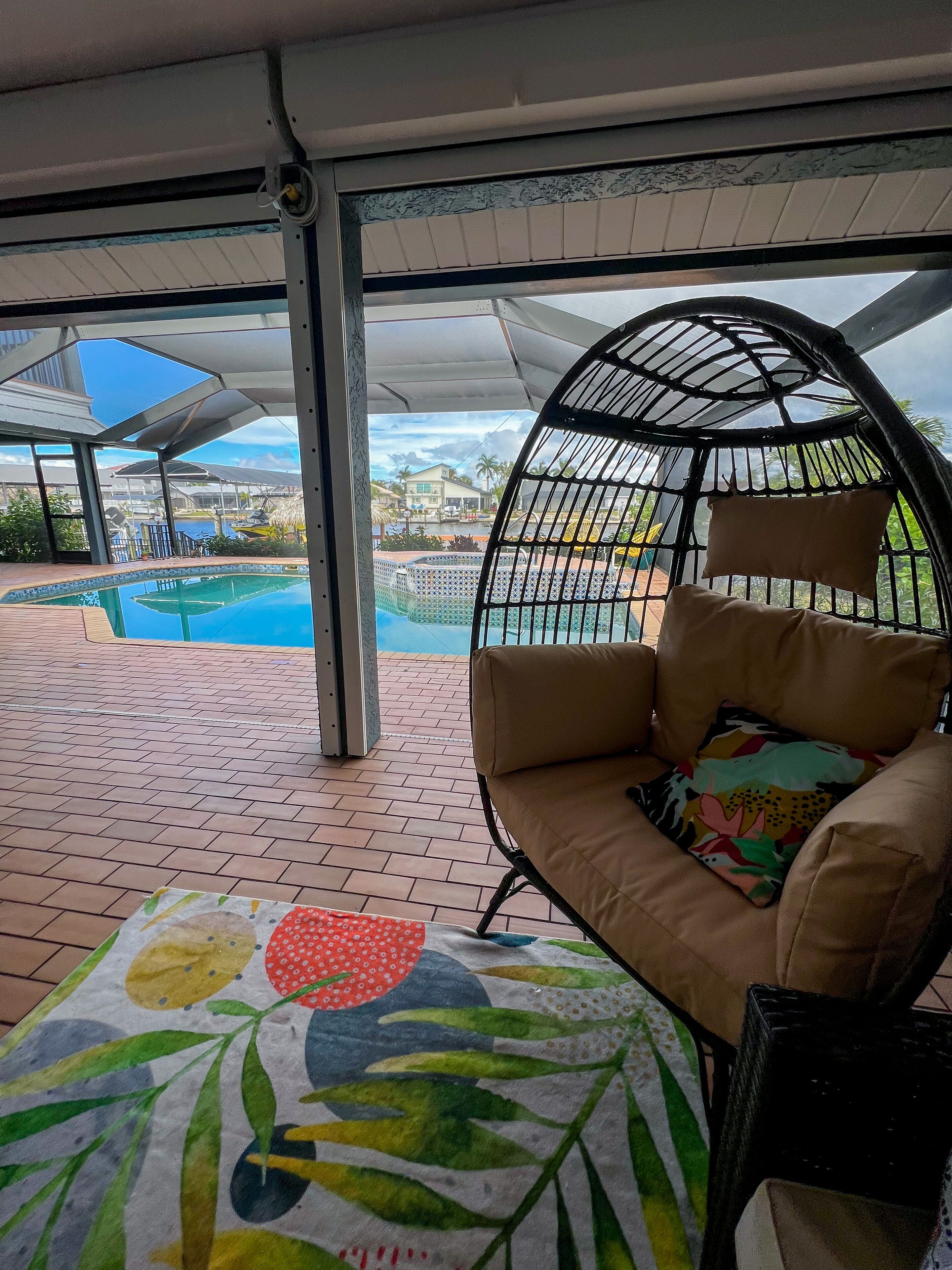 Un área de estar al aire libre techada con vista a una piscina y una casa al fondo.