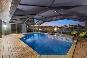 An outdoor swimming pool with a tiled edge, a hot tub, and yellow chairs under a covered area. - Gulf Access ☀️6BR ☀️Heated Pool ☀️Spa☀️Dock ☀️Tiki Hut ☀️Sleeps 11 (Cape Coral)