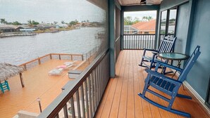 Eine Holzterrasse mit Blick auf ein Gewässer, ein Deckenventilator und ein Tisch mit Stühlen.