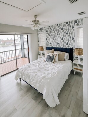A bedroom with a large bed, a ceiling fan, a patterned wall, and a view of the water outside. - Gulf Access ☀️6BR ☀️Heated Pool ☀️Spa☀️Dock ☀️Tiki Hut ☀️Sleeps 11 (Cape Coral)