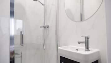 A modern bathroom with a glass-enclosed shower, a round mirror, and a white sink with a black cabinet.