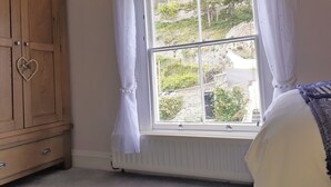 Een slaapkamer met een houten garderobe, een raam met witte gordijnen en uitzicht op een heuvel.