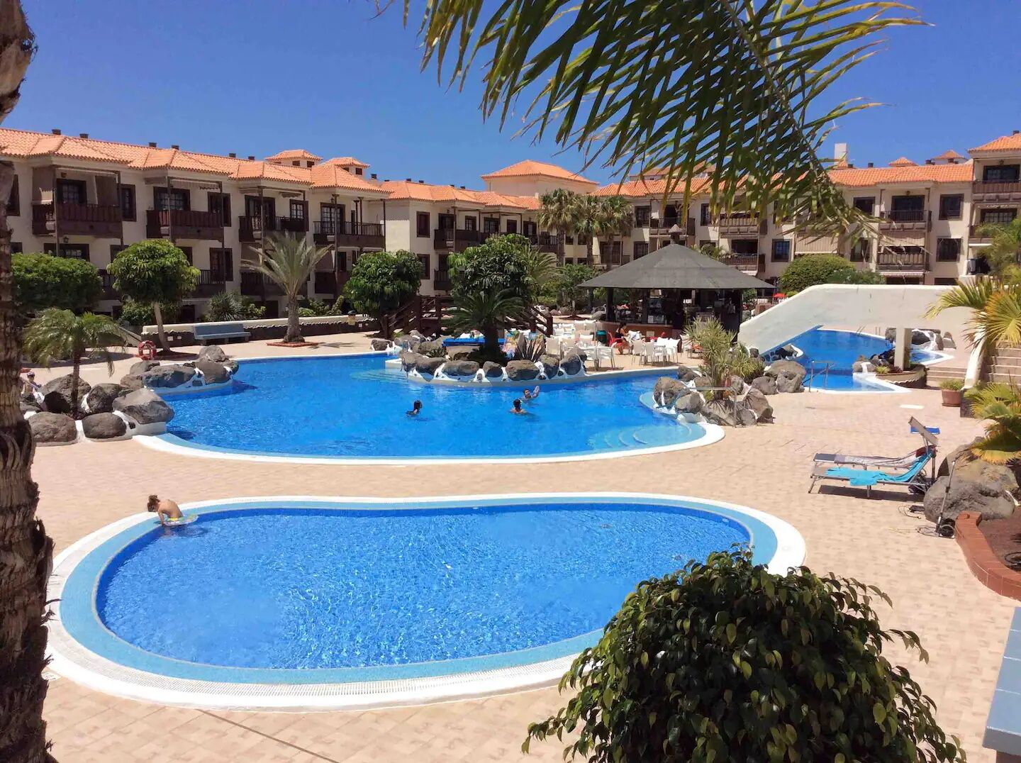 A resort with multiple swimming pools, palm trees, and a building with red-tiled roofs.