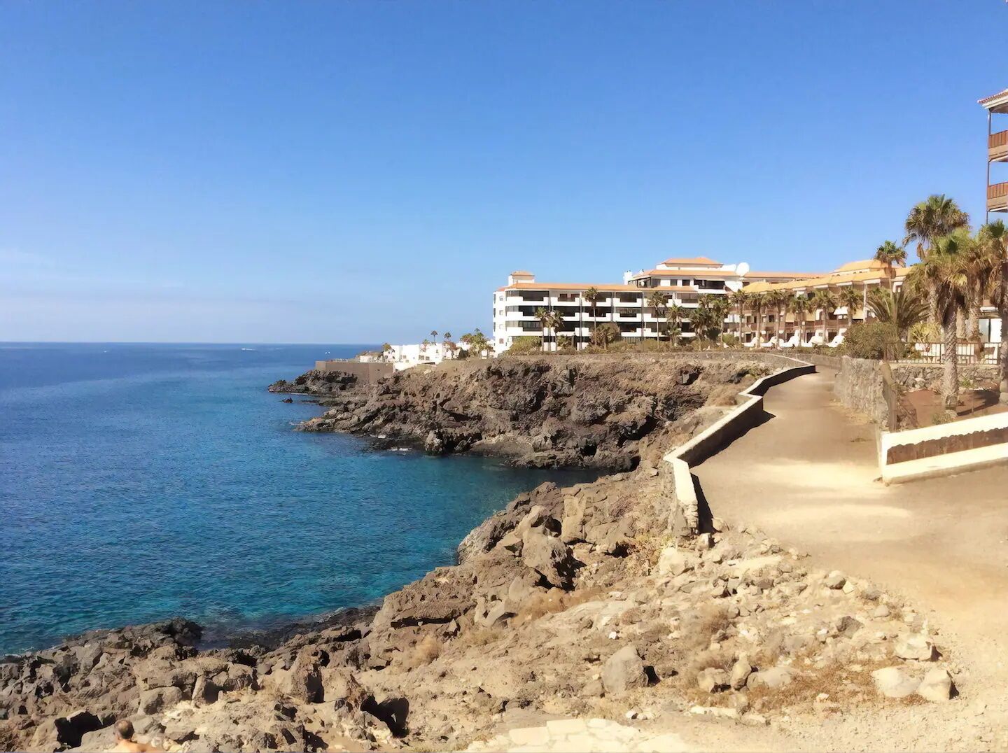 Un hotel frente al mar con un litoral rocoso, un paseo marítimo pavimentado y una vista despejada del océano.