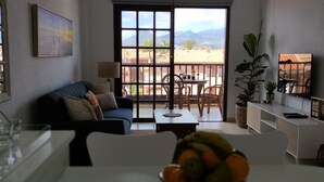 Un salon avec un canapé, une table basse et un saladier rempli de fruits. Il y a un balcon avec une table et des chaises.