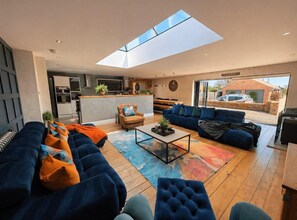 A modern living room with a large sofa set, a coffee table, and a skylight.
