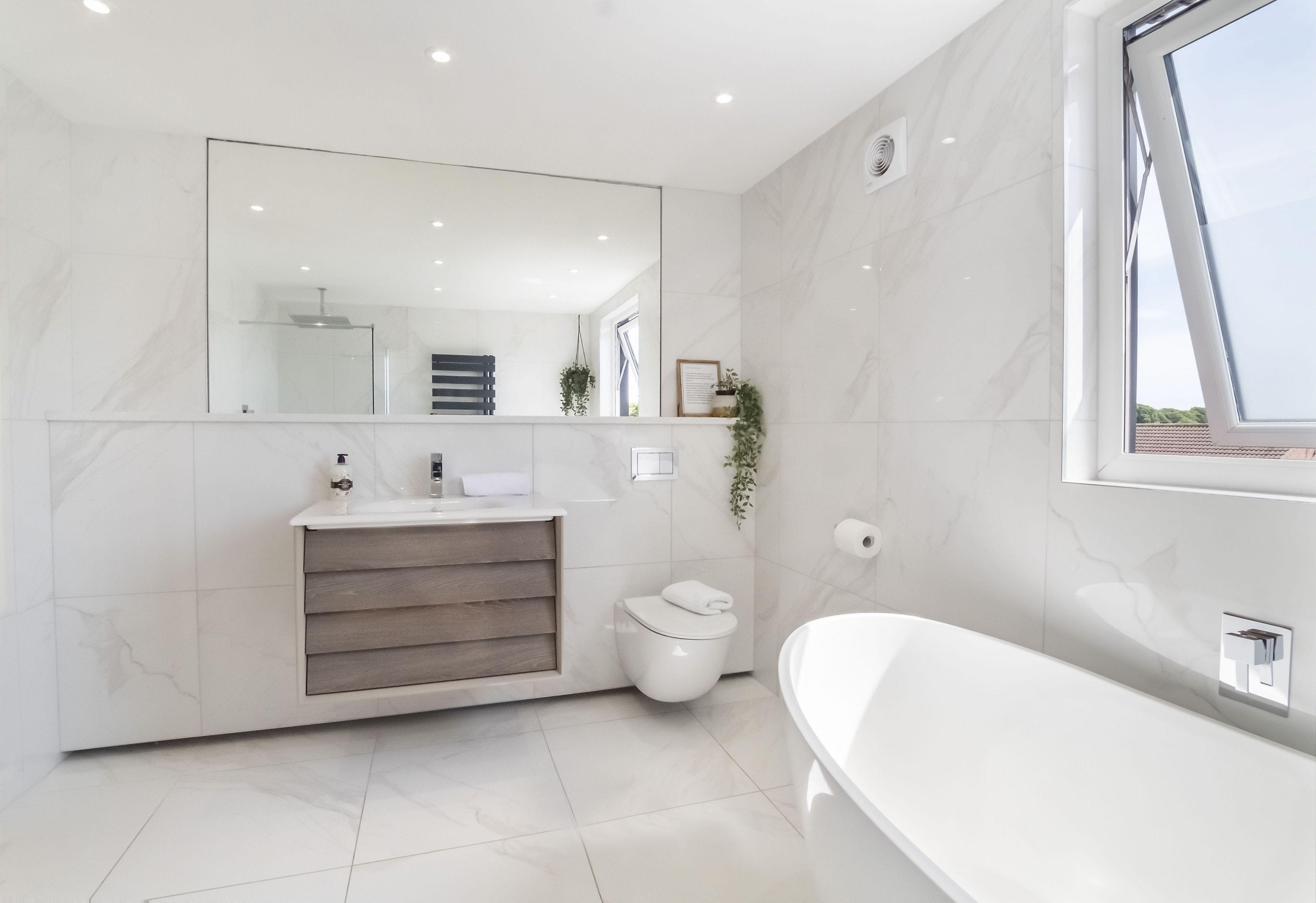 A modern bathroom with a large mirror, a freestanding bathtub, a toilet, and a vanity with a sink and towel rack.