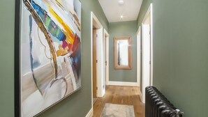 Un pasillo con un cuadro abstracto de gran tamaño, suelo de madera, un radiador y una puerta que da a otra habitación.