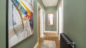 Un couloir avec un grand tableau abstrait, un plancher en bois, un radiateur et une porte donnant sur une autre pièce.