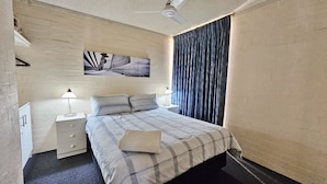 Una camera da letto con un letto, due comodini con lampade, una ventola a soffitto, un quadro appeso al muro e una finestra con tende.