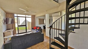 Sala de estar com sofá, televisão, ventilador de teto e escada.