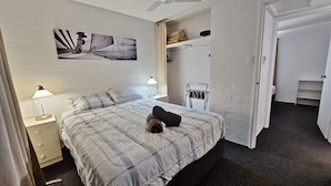 Cama bem arrumada com edredom xadrez, abajur e obra de arte na parede retratando um veleiro.