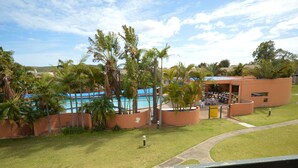 Zona de piscina con palmeras, un área de estar cubierta y un edificio con puerta amarilla.