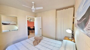 A bedroom with a bed, a ceiling fan, a bedside table with a lamp, a mirror, and a door leading to a dining area.