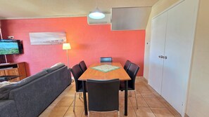 A dining area with a table, chairs, a sofa, a TV, and a lamp.