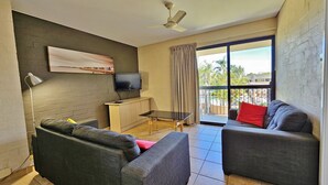 A living room with two sofas, a TV, a ceiling fan, and a balcony with curtains. - Riverview Holiday Apartment 66 -1st floor- Kalbarri WA (KALBARRI)