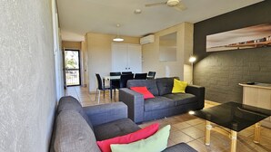 A living room with a sofa, armchair, and a glass coffee table. There is a dining area with a table and chairs in the background. - Riverview Holiday Apartment 66 -1st floor- Kalbarri WA (KALBARRI)