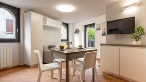 Une cuisine moderne avec des meubles blancs, une table à manger avec des chaises, une machine à café et un téléviseur fixé au mur.