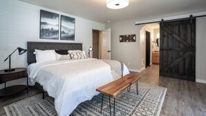 Een slaapkamer met een bed, nachtkastjes, een bankje, een kamerkleed met een patroon, en een schuifdeur in boerderijstijl.