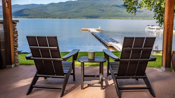 Twee Adirondack stoelen gericht op een meer met een steiger en bergen op de achtergrond.