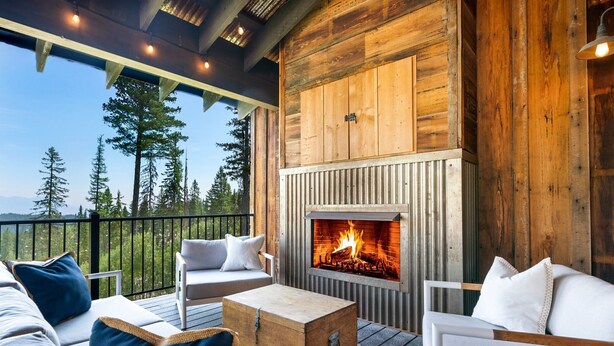 A cozy outdoor seating area with a fireplace, wooden deck, and a view of trees.