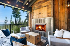Un espace extérieur accueillant avec un foyer, une terrasse en bois et une vue sur les arbres.