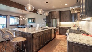 A modern kitchen with dark wood cabinets, a large island with bar stools, stainless steel appliances, and pendant lighting.