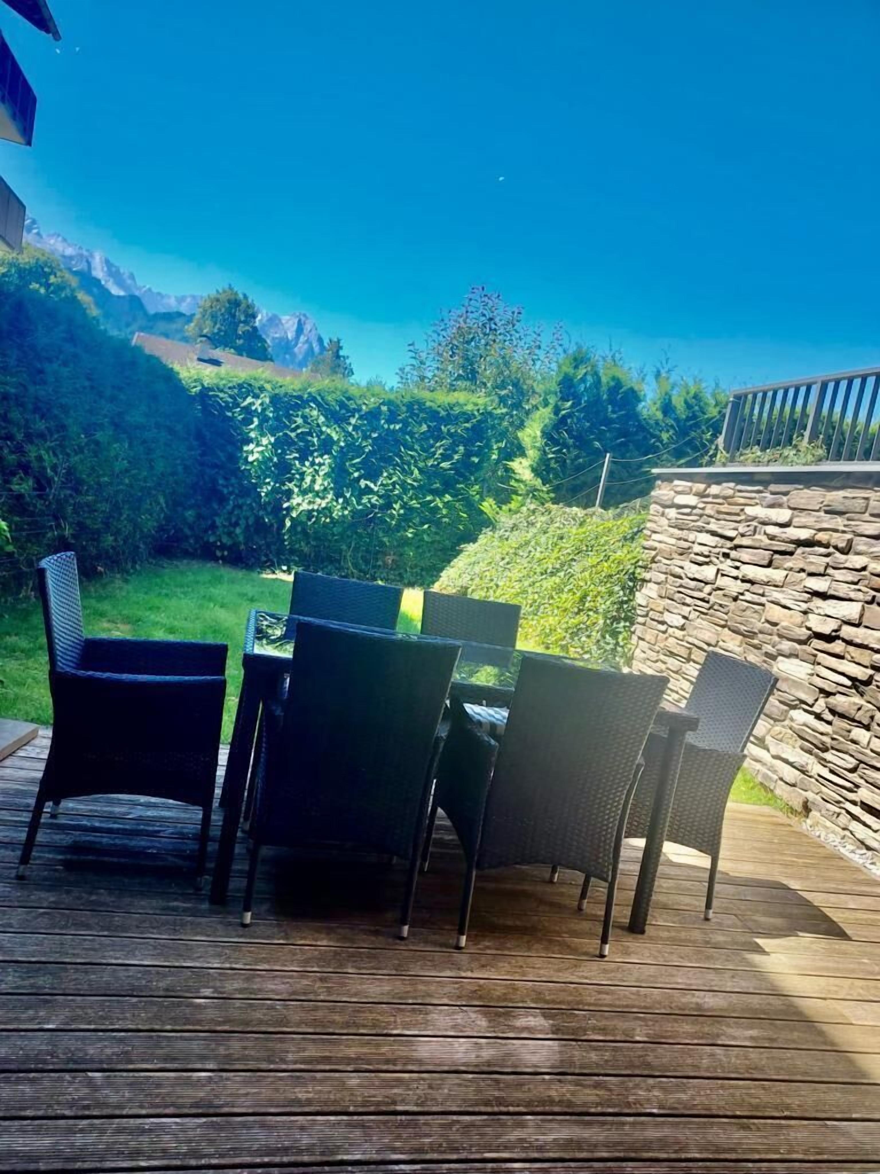 A deck with outdoor furniture and a stone wall, overlooking a landscaped garden and distant mountains.