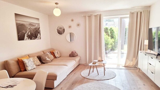Un salon moderne avec un canapé, une table à manger, un téléviseur et une vue sur la verdure à l’extérieur.