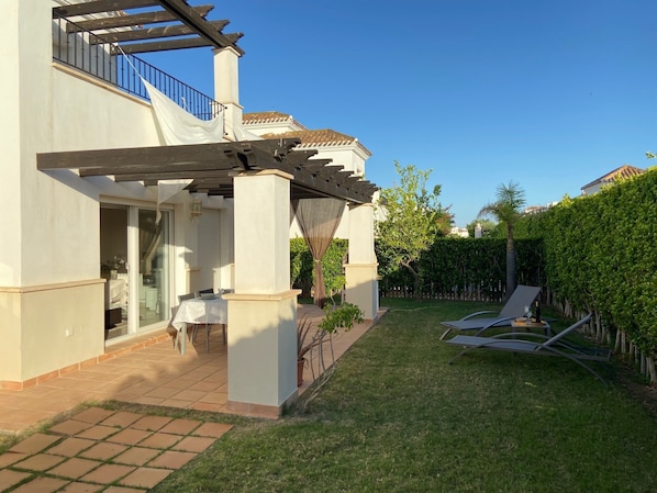 A modern house with a covered patio, a dining area, and a well-maintained lawn.