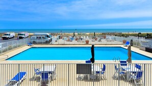 A pool area with a view of the beach, lounge chairs, and a lifeguard tower.