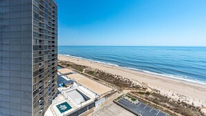 A high-rise hotel overlooking a beach with a pool and parking area.