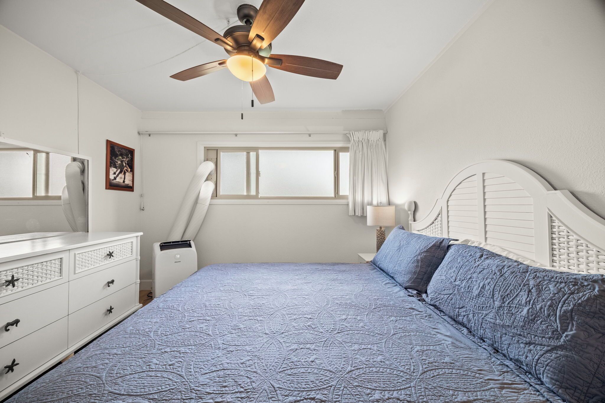 A bedroom with a bed, a ceiling fan, a window, and a dresser.