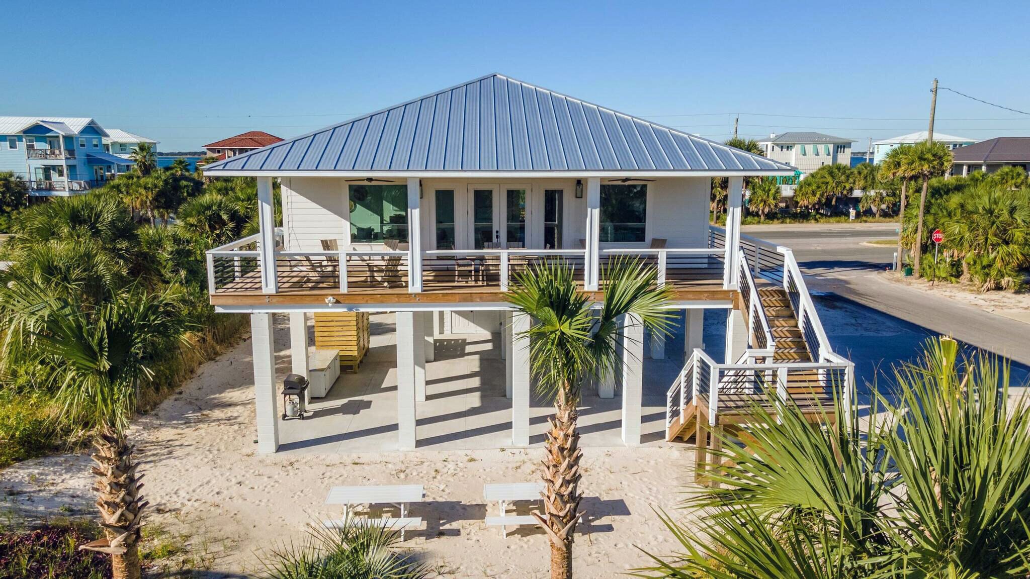 A beachfront house with a covered deck, a pool, and a sandy beach area.