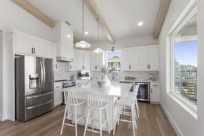 Una cocina moderna con armarios blancos, electrodomésticos de acero inoxidable y una isla central con taburetes de bar.