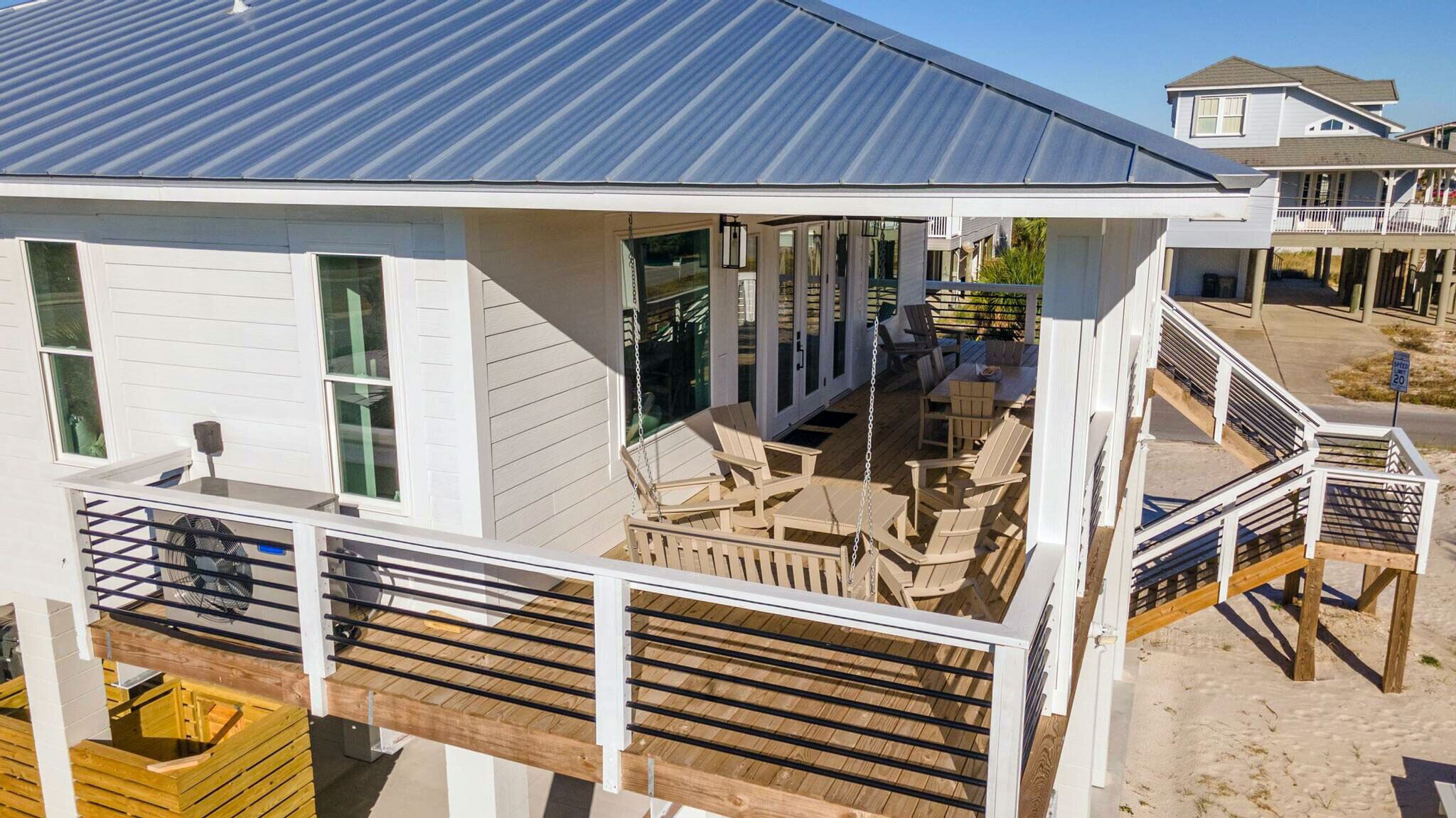 A beachfront house with a covered patio, outdoor seating, and a wooden deck.