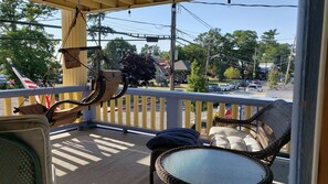 Un balcon avec des meubles en osier, un panneau de signalisation indiquant un arrêt obligatoire, et une vue sur une rue bordée d’arbres et où circulent des voitures.