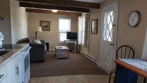 Una sala de estar con sofá, televisión y comedor con una silla y una mesa.