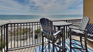 Ein Balkon mit Blick auf den Strand, mit zwei Adirondack-Stühlen und einem kleinen Tisch.