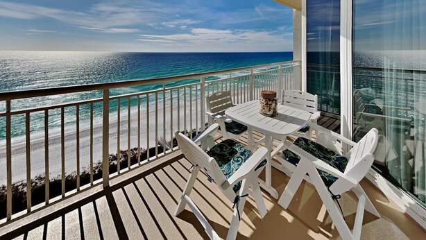 Een balkon met een tafel en stoelen met uitzicht op een strand en zee.