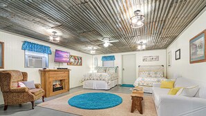 A room with a fireplace, two beds, a sofa, a chair, and a ceiling fan. - Come On Inn | Close to Downtown Wimberley! (Wimberley)